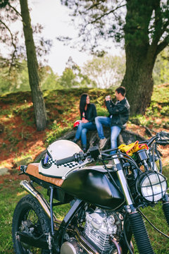 Custom motorbike with young couple resting from a motorcycle trip in background. Selective focus on motorbike in foreground