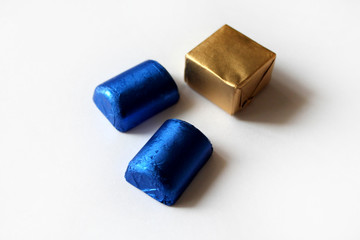 Chocolate candies wrapped in blue and golden foil isolated on white surface. Template for greeting card, poster or invitation. Sweets scattered on white smooth table. Backdrop or background