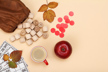 Wooden lotto barrels with bag, game cards, apple and cup of coffee on beige background. Autumn theme.
