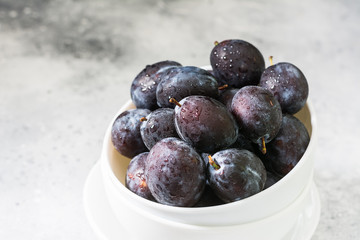 Juicy plums in white dishes on a light grey table