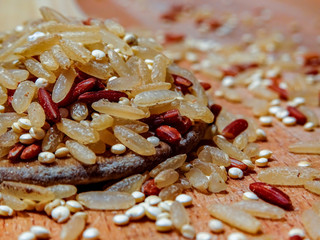 Mix red rice, complete rice, quinoa uncooked on wooden spoon and wooden surface 