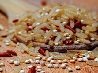 Mix red rice, complete rice, quinoa uncooked on wooden spoon and wooden surface 