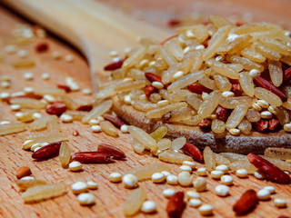 Mix red rice, complete rice, quinoa uncooked on wooden spoon and wooden surface 