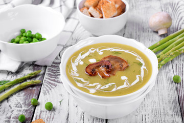Vegetable cream soup with asparagus and peas garnished with cream and roasted champignons
