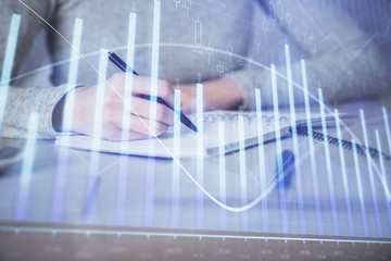 Hands writing information about stock market in notepad. Forex chart holograms in front. Concept of research. Multi exposure