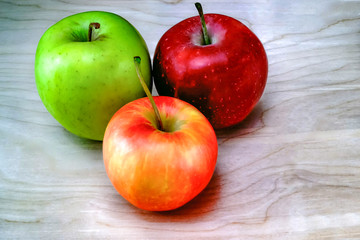 Red, green and yellow-red apples on a wooden table, the background is a table made of light oak. close up