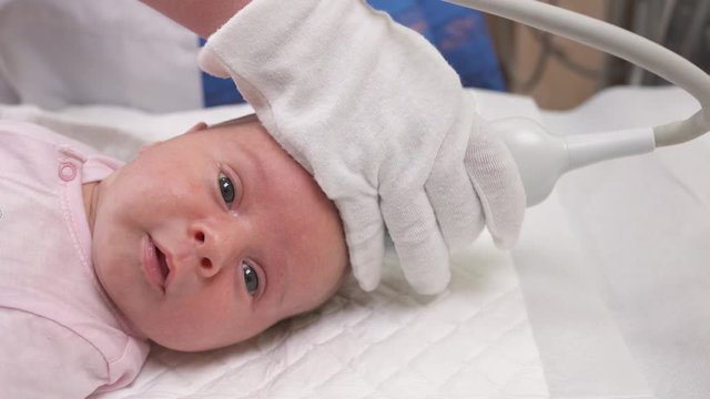 A close-up of the adorable infant baby lying on a white sheet during ultrasound fontanels check-up. Neonatology. Healthcare concept