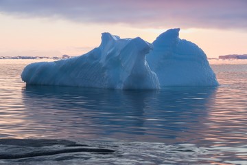 Fototapeta na wymiar Arctic nature landscape with icebergs in Greenland icefjord with midnight sun sunset / sunrise in the horizon. Early morning summer alpenglow during midnight season. Ilulissat, West Greenland.