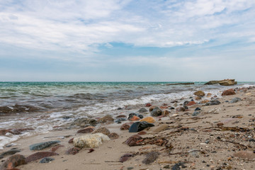 Stony Baltic Sea coast with pebbles, waves and clouds blue sky