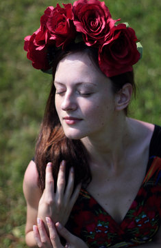 View of a beautiful, dreaming girl with closed eyes, who has a beautiful red wreath on her head with large flowers.