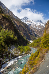 A picturesque valley with mountain river and snow-covered tops of the mountains in the Nepalese Himalayas on the Annapurna Circuit trek.