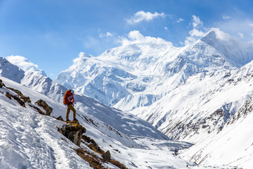 Strong girl with backpack Osprey stands on the edge of the mountain overlooking the snow-capped peaks of the Himalayas on Annapurna Circuit Trek in Nepal. - obrazy, fototapety, plakaty