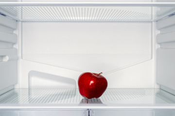 One red Apple on the shelf of an empty fridge. Weight loss, diet and hunger concept
