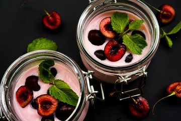 selective focus, still life, Breakfast. cherry pink yogurt in a glass jar with ripe cherries and green mint leaves