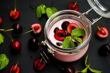 selective focus, still life, Breakfast. cherry pink yogurt in a glass jar with ripe cherries and green mint leaves