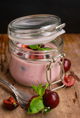 selective focus, still life, Breakfast. cherry pink yogurt in a glass jar with ripe cherries and green mint leaves