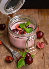 selective focus, still life, Breakfast. cherry pink yogurt in a glass jar with ripe cherries and green mint leaves