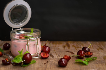 selective focus, still life, Breakfast. cherry pink yogurt in a glass jar with ripe cherries and green mint leaves