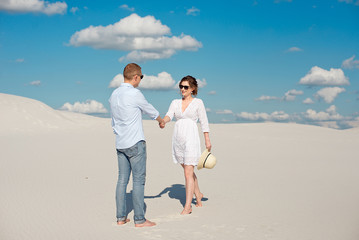 Young couple enjoying the sunset in the dunes. Romantic traveler walks in the desert. Adventure travel lifestyle concept.