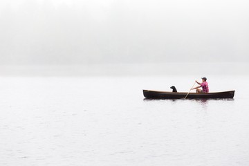 Wide shot of a male with black dog riding boat on a lake
