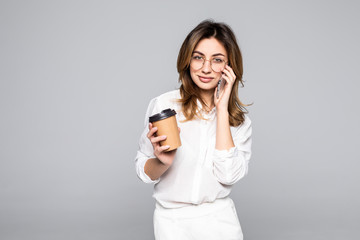 Young business woman posing talking by mobile phone drinking coffee isolated over grey wall background
