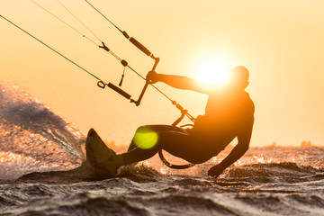 Silhouette of kitesurfer riding in beautiful sunset conditions with sun next to the riders head - obrazy, fototapety, plakaty
