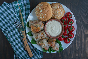 Spring roll with meat and vegetables served on a white dish with sauce. Dark wooden background.
