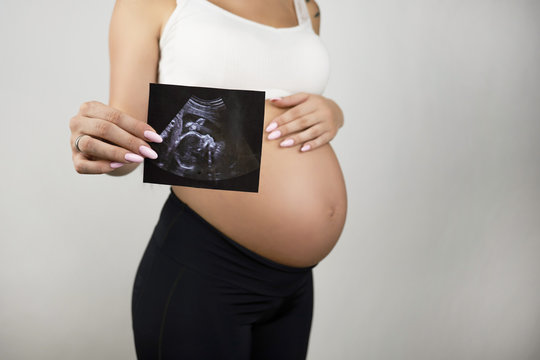 pregnant woman holding ultrasound picture of her baby standing half a turn on isolated white background