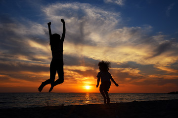 Happy young family have fun on beach and jump at sunset. Silhouette of mom and son jump at sunset