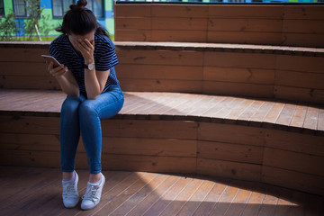 Young girl, brunette with long hair, with a phone in her hand, is crying, covering face with hands,...