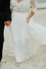 Fototapeta na wymiar Bride and groom walking on beach, bride holding dress, barefoot