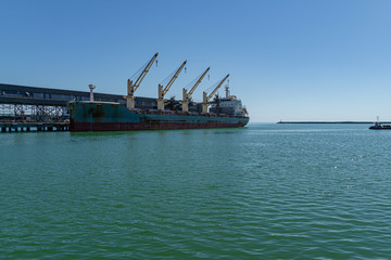 Large blue sea ship dry cargo ship or bulk carrier near bulk terminal in the emerald waters of the Black Sea. Sunny day