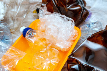 Lot of used plastic, orange container plate, crumpled empty bottles, packets, pollution recycle eco concept background close up selective focus