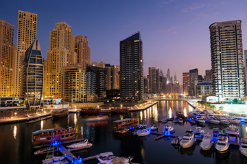 Obraz premium Dubai marina with boats and buildings with gates at night with lights and blue sky, United Arab Emirates