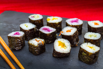 Several pieces of vegetable hosomaki sushi on a slate plate with chopsticks.