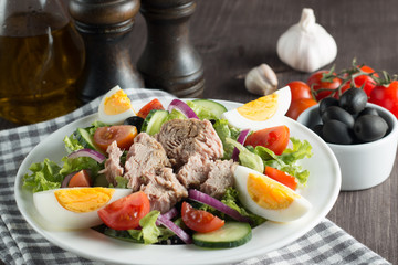 Fresh Caesar tuna salad with delicious tuna fish, ruccola, spinach, cabbage, arugula, egg, parmesan and cherry tomato on wooden background. Oil, salt and pepper. Healthy and diet food concept.