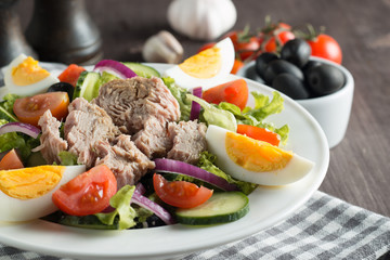 Fresh Caesar tuna salad with delicious tuna fish, ruccola, spinach, cabbage, arugula, egg, parmesan and cherry tomato on wooden background. Oil, salt and pepper. Healthy and diet food concept.