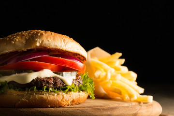 Home made hamburger with beef, onion, tomato, lettuce and cheese. Fresh burger close up on wooden rustic table with potato fries, beer and chips. Cheeseburger.