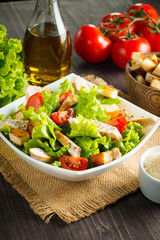 Fresh salad with delicious chicken breast, ruccola, spinach, cabbage, arugula and tomato on wooden background. Oil, salt and pepper.