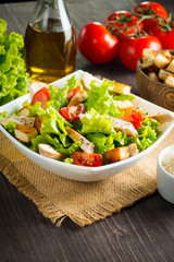 Fresh salad with delicious chicken breast, ruccola, spinach, cabbage, arugula and tomato on wooden background. Oil, salt and pepper.