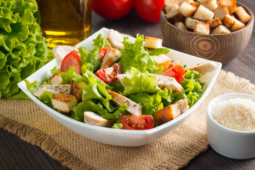 Fresh salad with delicious chicken breast, ruccola, spinach, cabbage, arugula and tomato on wooden background. Oil, salt and pepper.