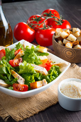 Fresh salad with delicious chicken breast, ruccola, spinach, cabbage, arugula and tomato on wooden background. Oil, salt and pepper.