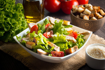 Fresh salad with delicious chicken breast, ruccola, spinach, cabbage, arugula and tomato on wooden background. Oil, salt and pepper.