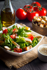Fresh salad with delicious chicken breast, ruccola, spinach, cabbage, arugula and tomato on wooden background. Oil, salt and pepper.