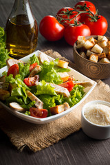 Fresh salad with delicious chicken breast, ruccola, spinach, cabbage, arugula and tomato on wooden background. Oil, salt and pepper.