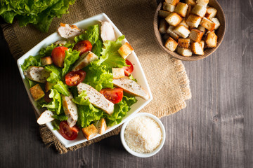 Fresh salad with delicious chicken breast, ruccola, spinach, cabbage, arugula and tomato on wooden background. Oil, salt and pepper.
