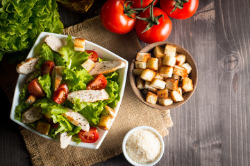 Fresh salad with delicious chicken breast, ruccola, spinach, cabbage, arugula and tomato on wooden background. Oil, salt and pepper.