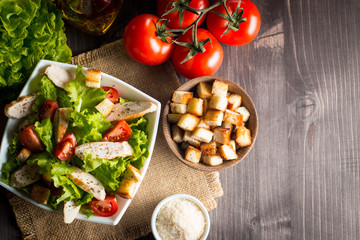 Fresh salad with delicious chicken breast, ruccola, spinach, cabbage, arugula and tomato on wooden background. Oil, salt and pepper.