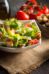 Fresh salad with delicious chicken breast, ruccola, spinach, cabbage, arugula and tomato on wooden background. Oil, salt and pepper.