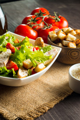 Fresh salad with delicious chicken breast, ruccola, spinach, cabbage, arugula and tomato on wooden background. Oil, salt and pepper.